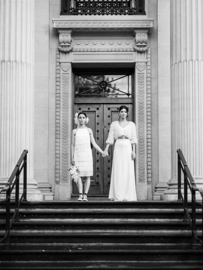 Two brides standing at the top of the Old Marylebone in London. Both are wearing two piece wedding dresses